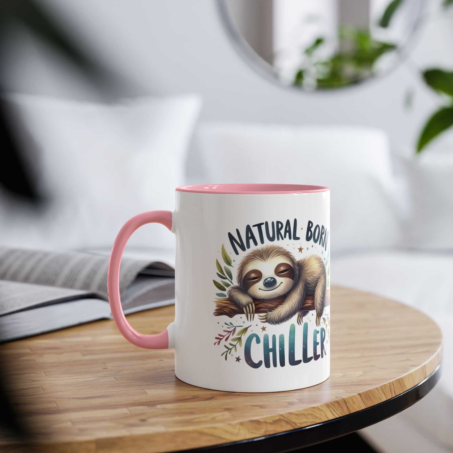 Cute sloth coffee mug with a pink handle and "Natural Born Chiller" printed on it, resting on a table.