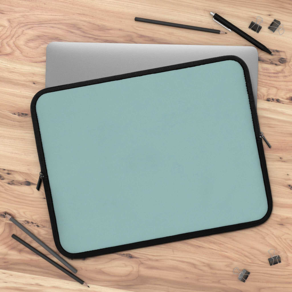 Teal green neoprene laptop sleeve with black trim on wooden desk