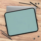 Teal green neoprene laptop sleeve with black trim on wooden desk