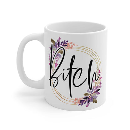 White ceramic mug with "Bitch" text in black script surrounded by a floral wreath, glossy finish, 11oz, microwave and dishwasher safe