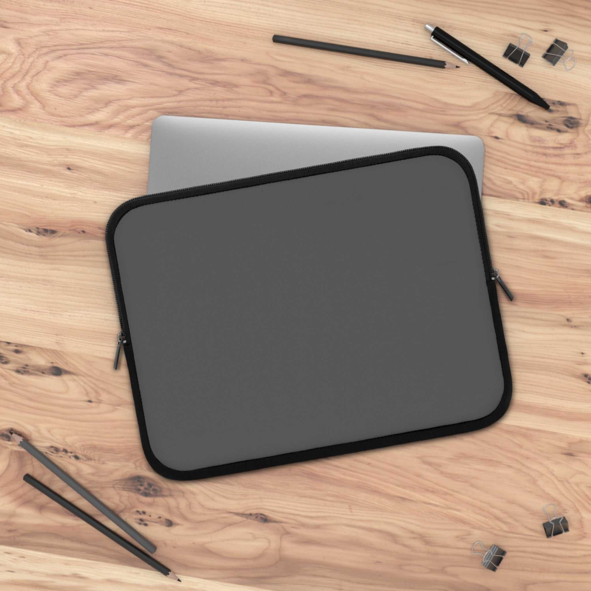 gunmetal grey neoprene laptop sleeve with dual zipper on wooden desk with pencils and clips
