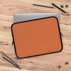Bold orange neoprene laptop sleeve with dual zipper and soft foam lining on wooden desk