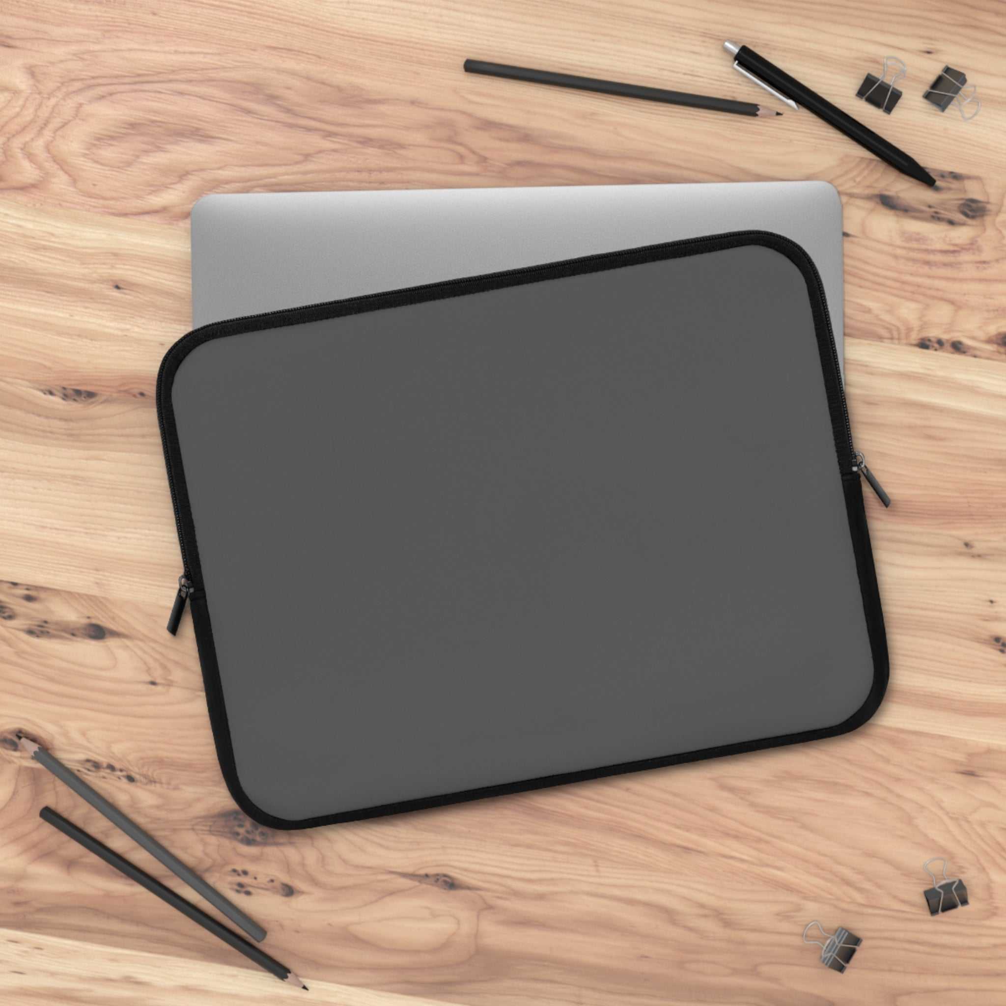 Gunmetal grey neoprene laptop sleeve with soft foam lining and dual zipper on wooden desk with pens and clips
