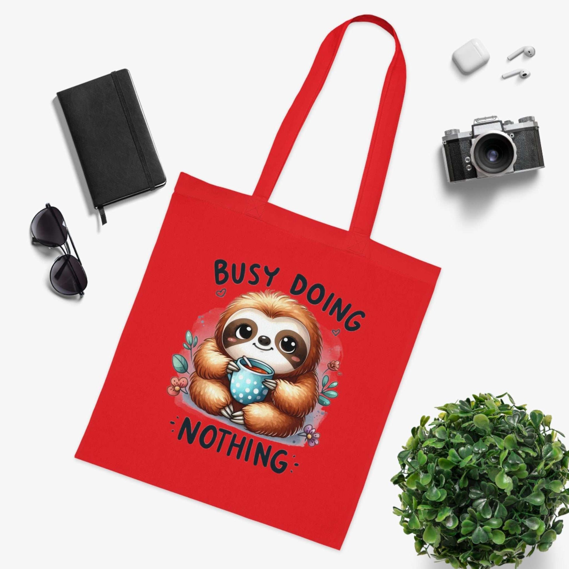 Red cotton tote bag featuring a cute sloth design with the text "Busy Doing Nothing," ideal for sloth lovers.