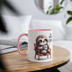 Cute sloth coffee mug with ceramic design and pink handle on wooden table.