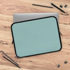 Teal green neoprene laptop sleeve with black trim, soft foam lining, dual zipper, lightweight and waterproof design on wooden surface