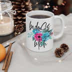 Badass Bitch Ceramic Mug with floral design, glossy finish, coffee-filled, surrounded by pine cones and cinnamon sticks.