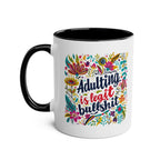 Black and white ceramic coffee mug with colorful floral design and text "Adulting Is Bullshit".