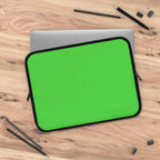 Lime green neoprene laptop sleeve with black trim, dual zipper, and soft foam lining for protection on wooden surface with office supplies