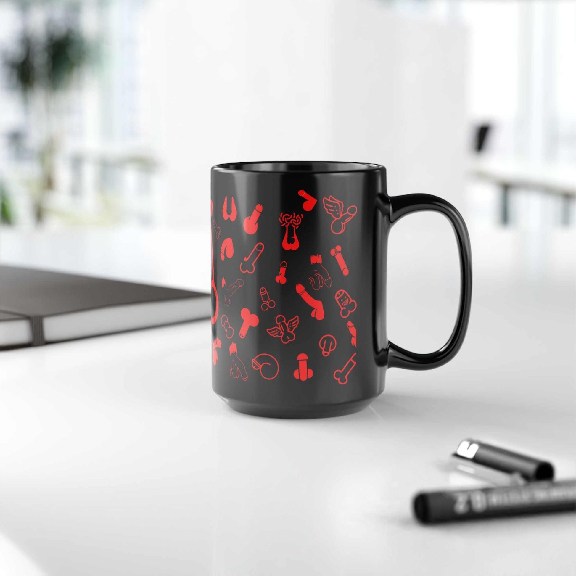 Black ceramic mug with playful red willies print, available in 11oz and 15oz sizes, on a desk.