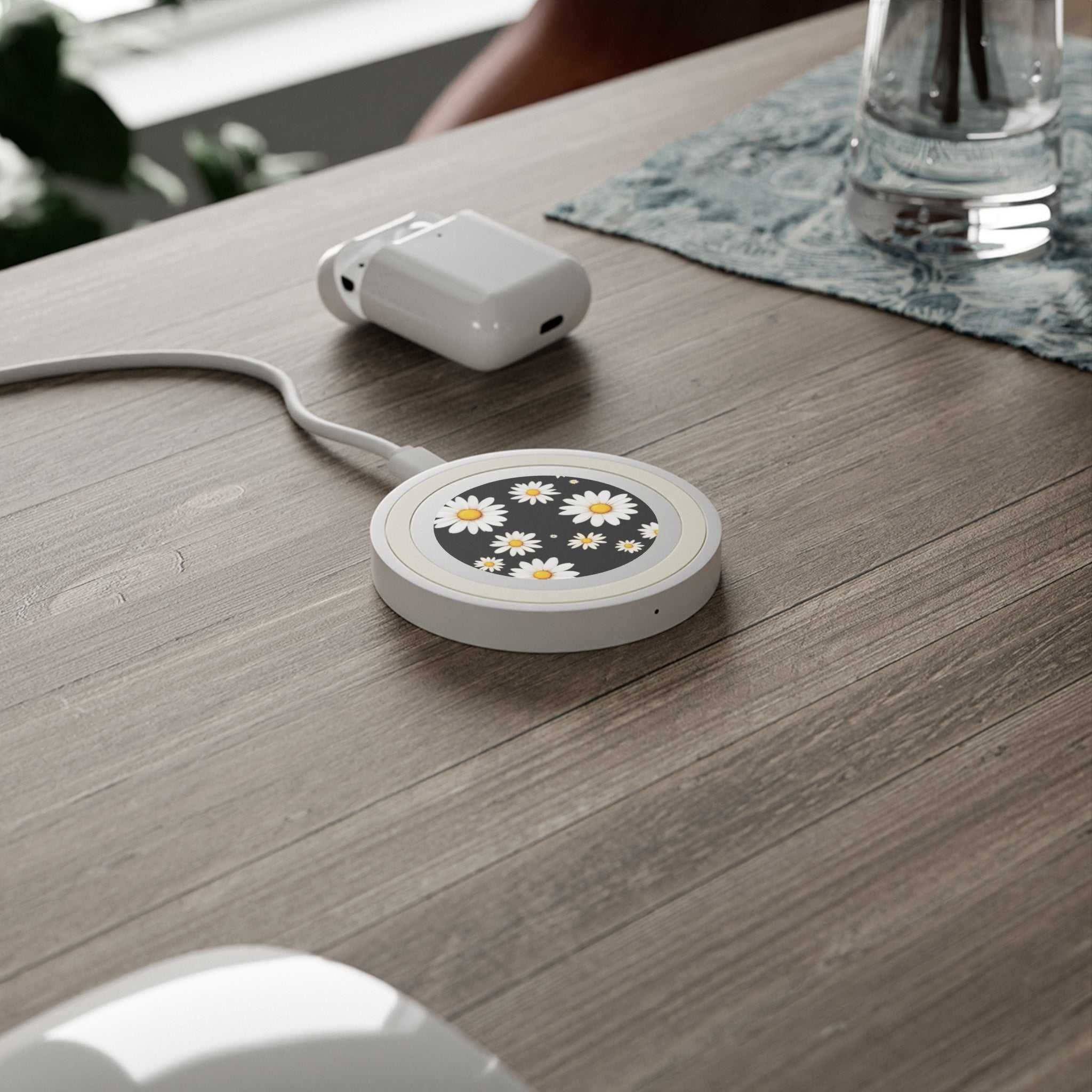 Black Daisy Design wireless charging pad with daisy pattern on a wooden desk with white charging cable and earbud case