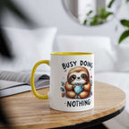 Cute sloth coffee mug with "busy doing nothing" text, yellow handle, 11oz ceramic, cheerful design.