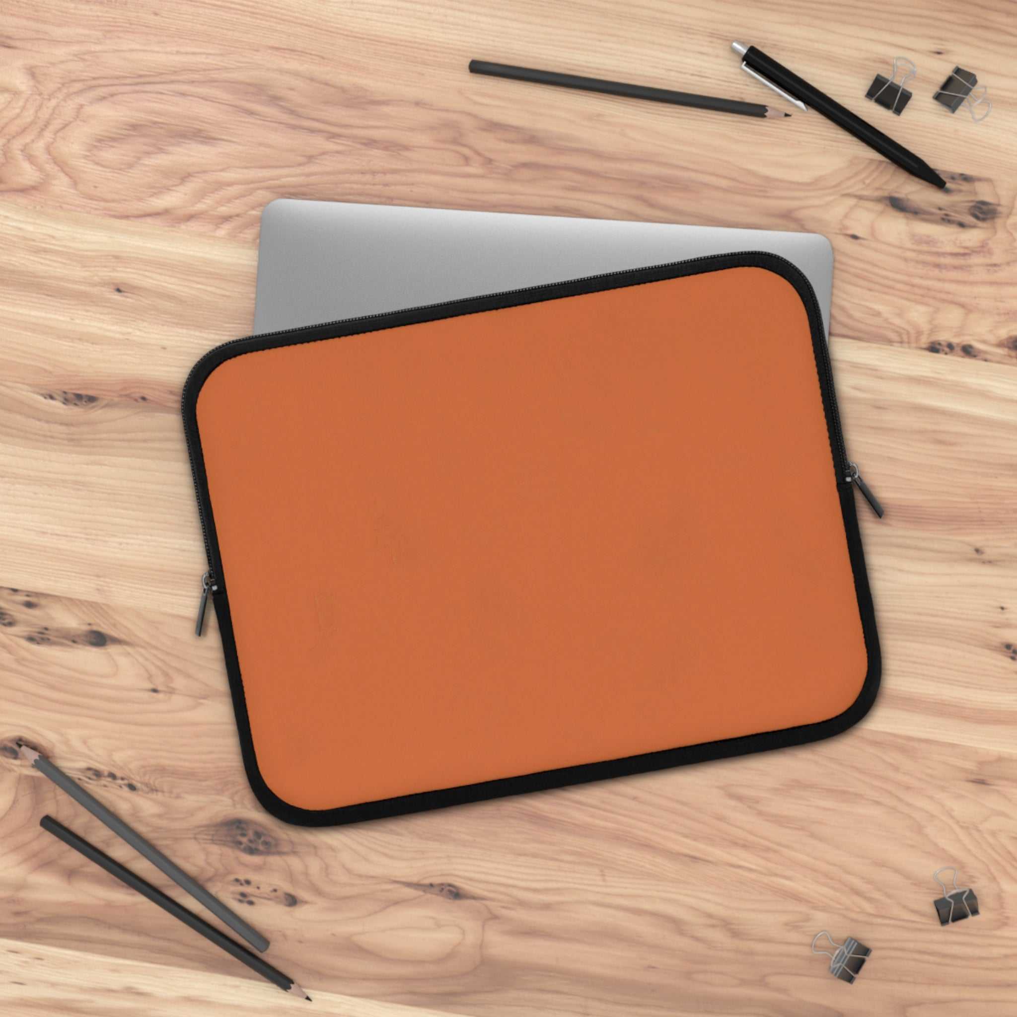 Bold orange neoprene laptop sleeve with soft foam lining and dual zipper on wooden desk