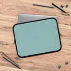 teal green neoprene laptop sleeve with black trim on wooden desk with pencils and clips