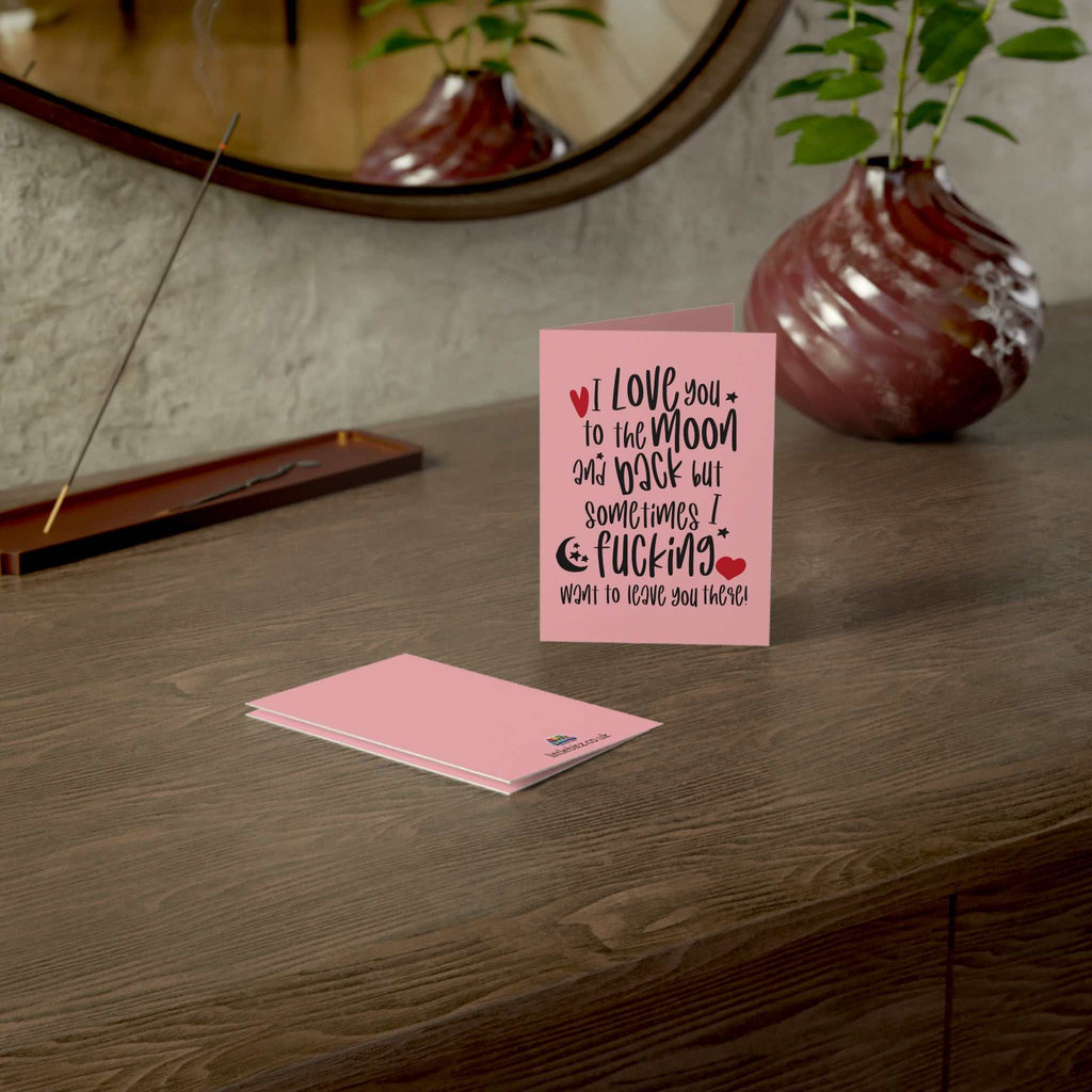Cheeky funny greeting card on a wooden table with a pink design and humorous text.