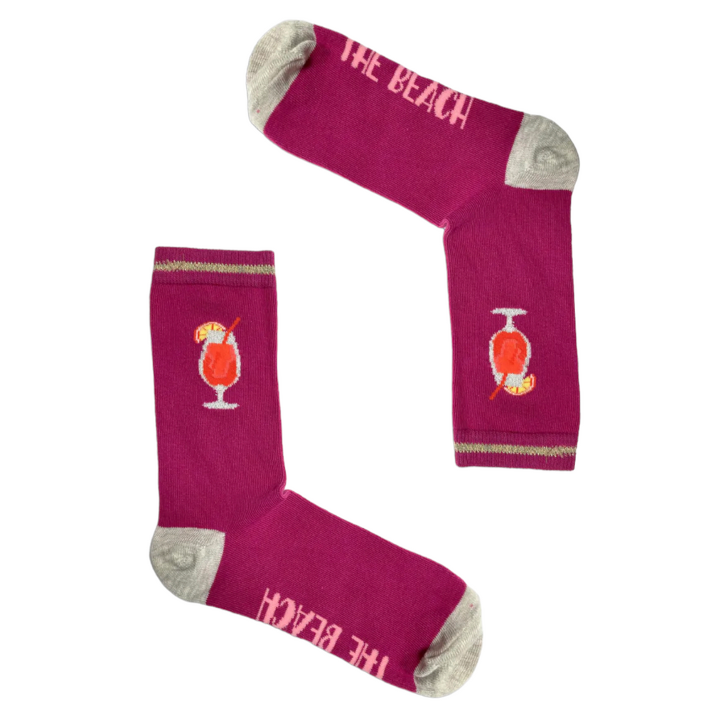 Bright pink mid-calf socks with grey heel and toe, cocktail drink design, and "The Beach" text, part of the Socktails Gift Set